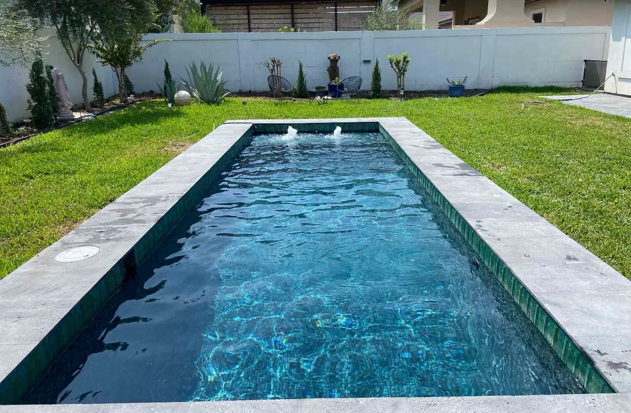 Dark-finish lap pool with deck jets set into a walled lawn behind a Laredo home