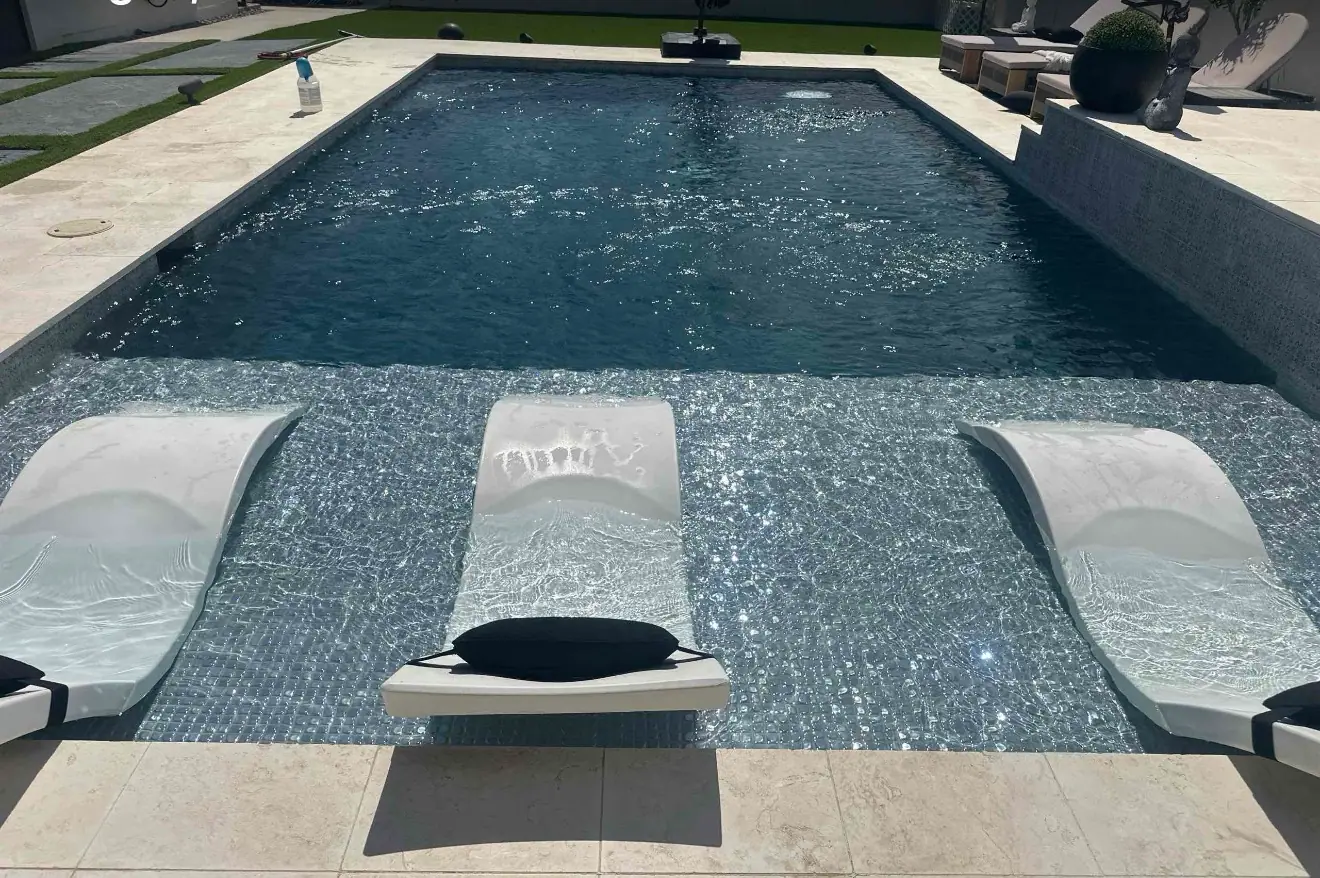 Finished JCW pool with a dark interior finish, tanning ledge and two in-water loungers on a travertine deck