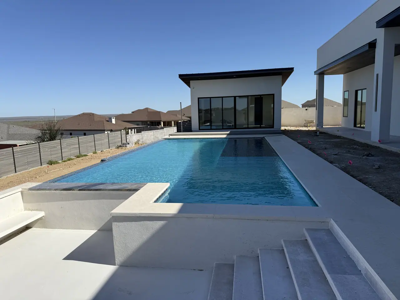 Newly finished rectangular pool with a tanning ledge and step entry behind a modern Laredo home