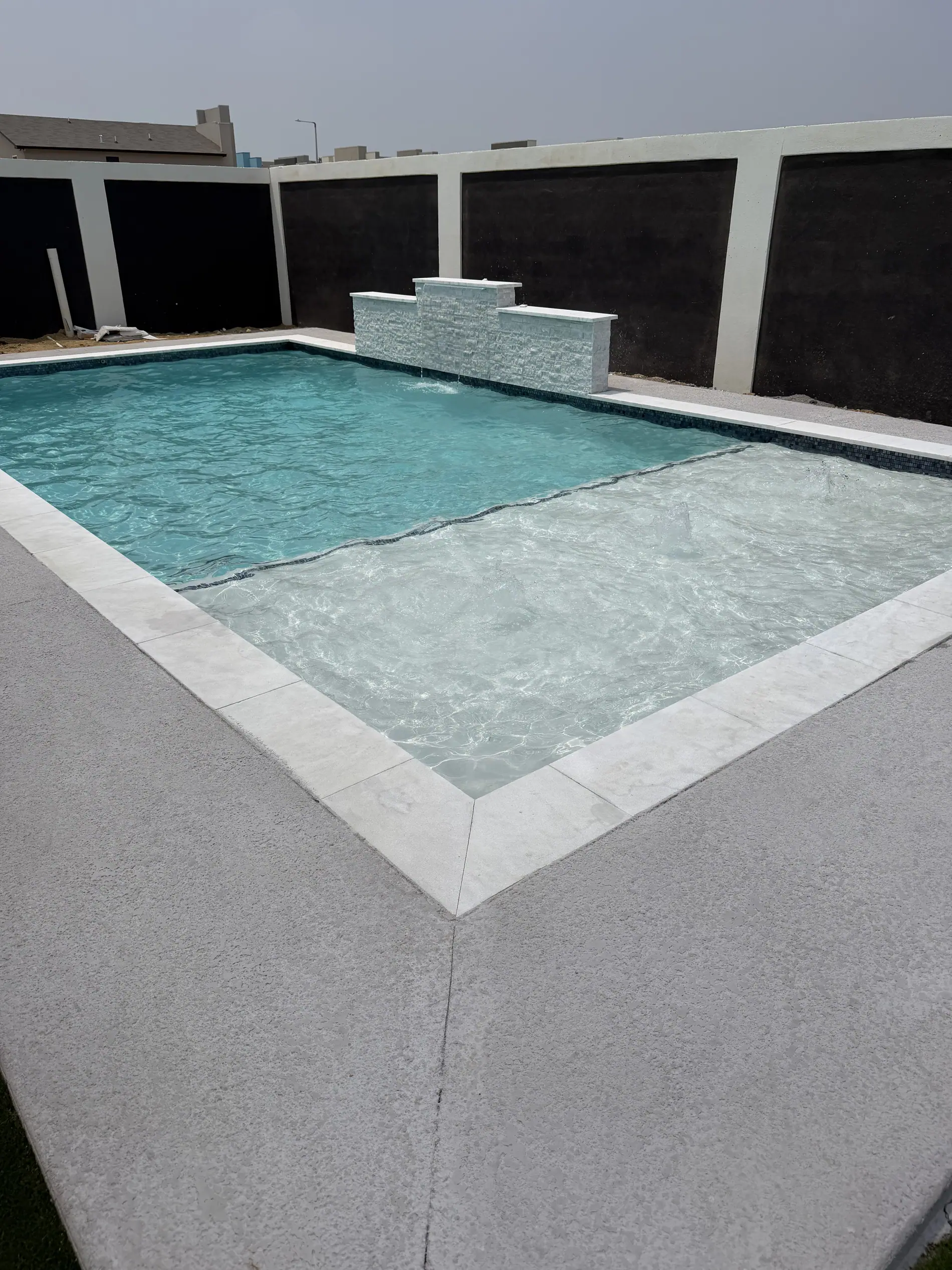 Modern JCW pool with a raised bond-beam wall and a sheer descent spillway in a minimal walled yard