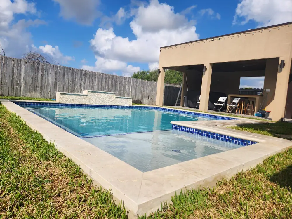 JCW pool with a raised spa, blue waterline tile and a covered cabana on a travertine deck