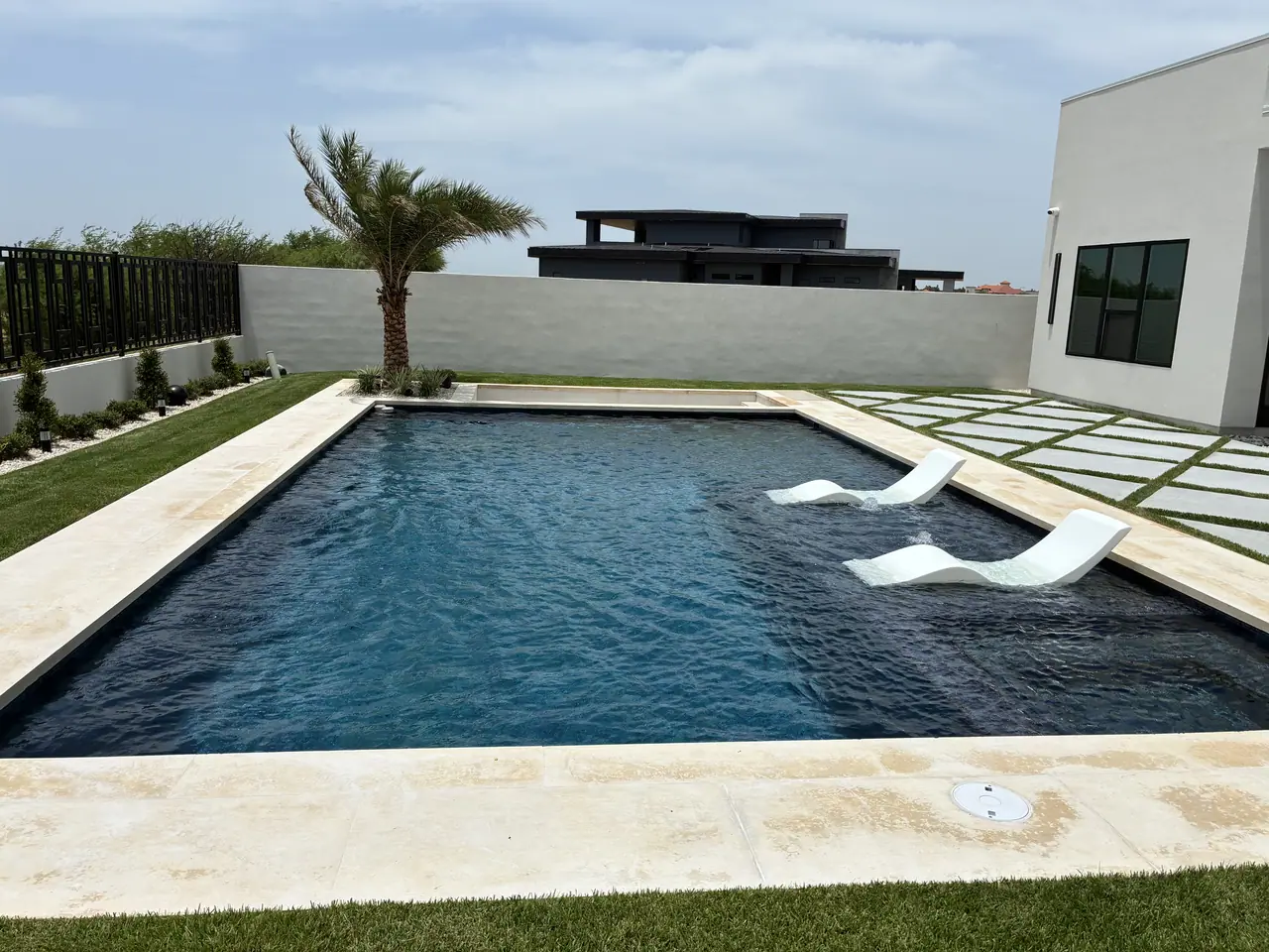 Rectangular JCW pool with dark water and white in-water loungers beside a white modern Laredo house