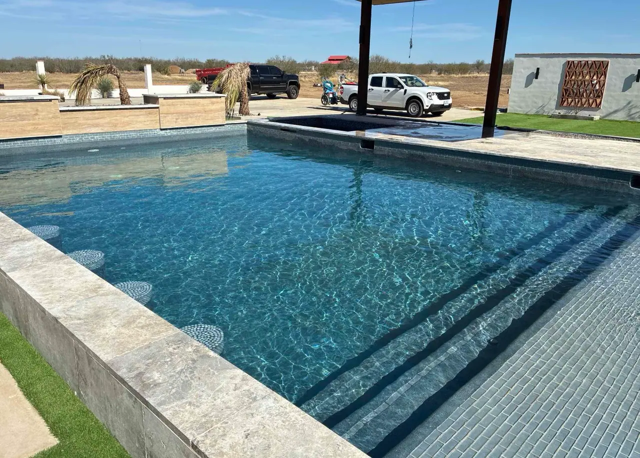 Corner of a JCW pool with clear water, a wide tanning ledge and open sky behind