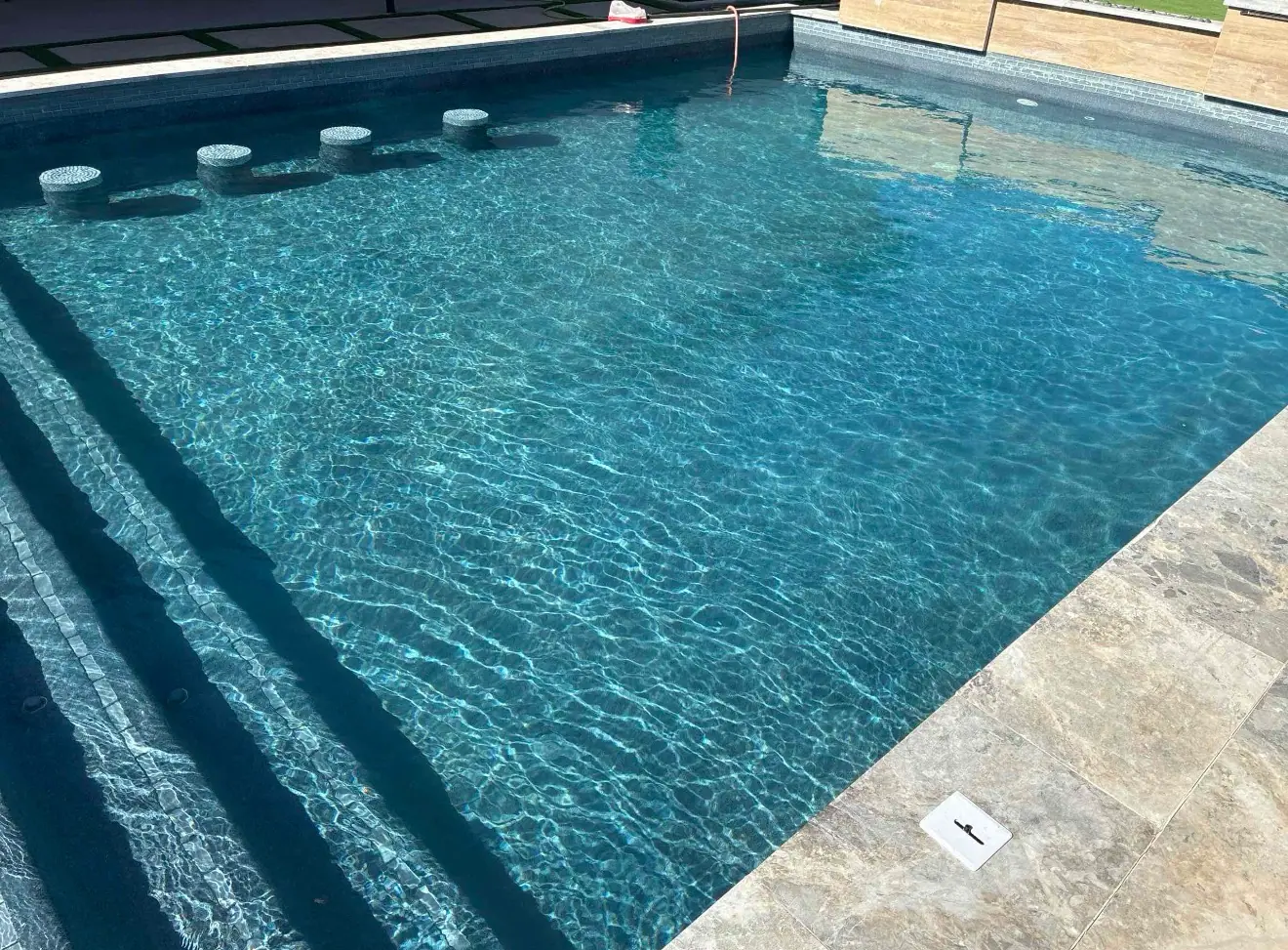 Sunlight sparkling across clear water in a JCW pool with step entry and travertine coping