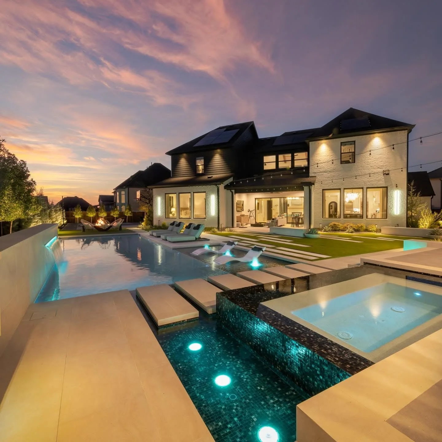 Pool and spa at dusk with lit steps, in-water loungers and the lit house behind