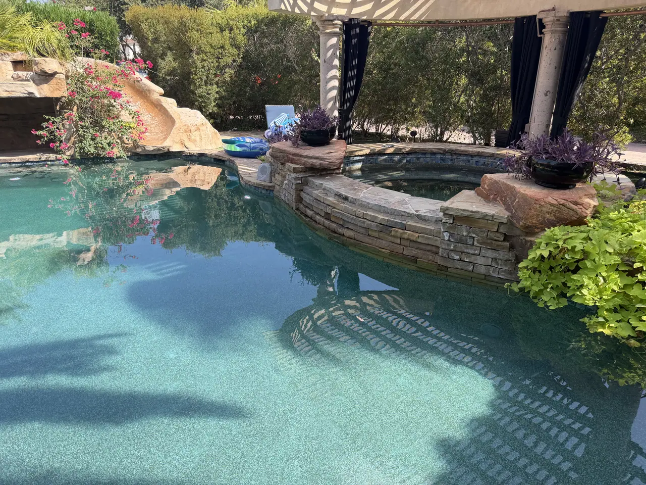 Rock grotto and waterfall feeding a freeform JCW pool with a curtained pergola alongside