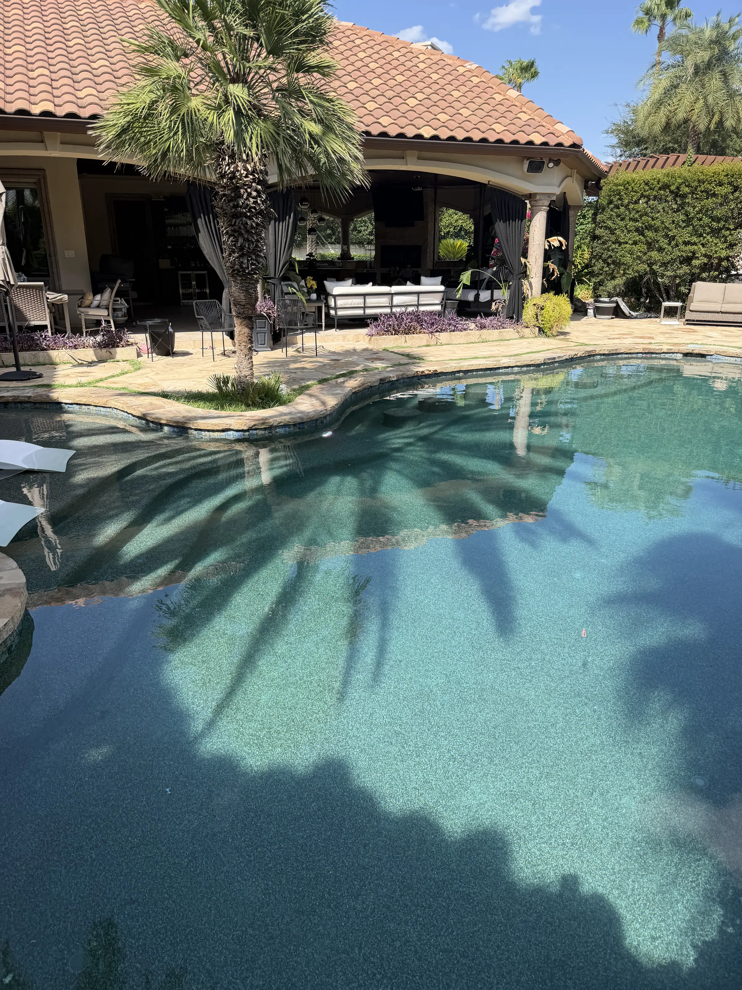 Resort-style JCW pool with palm shadows falling across clear turquoise water beside a hacienda