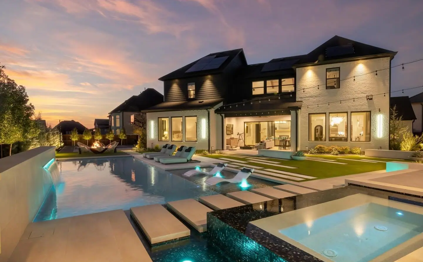 JCW pool and spa glowing at twilight behind a large Laredo home under a pink and blue sunset sky