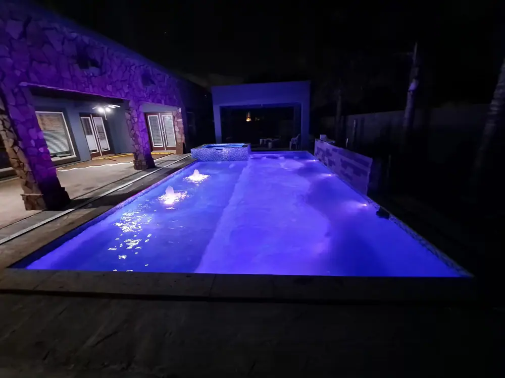 JCW pool glowing violet at night against a stone garden wall
