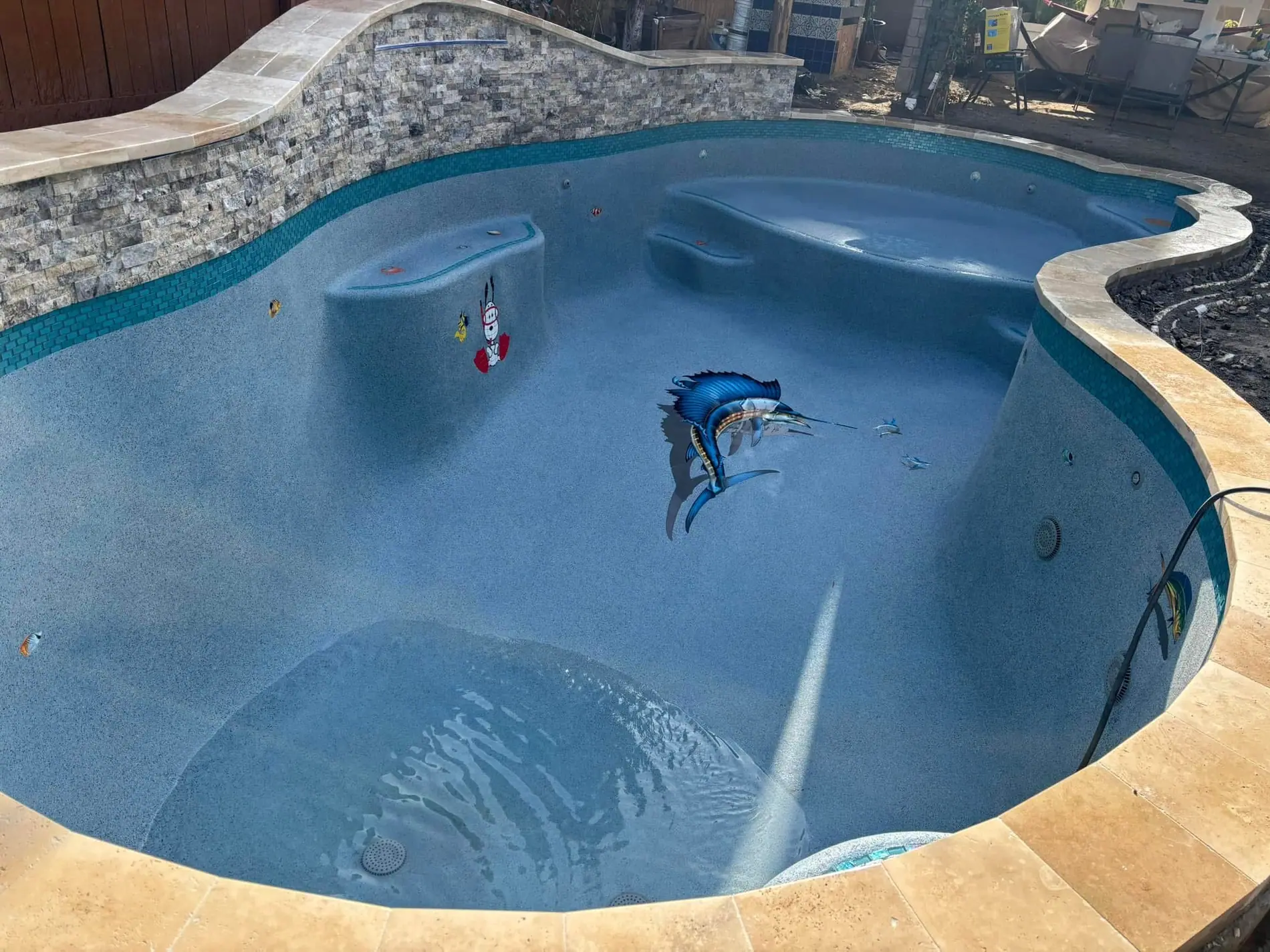 Remodeled freeform JCW pool with a marlin mosaic on the floor, stone waterfall wall and travertine coping