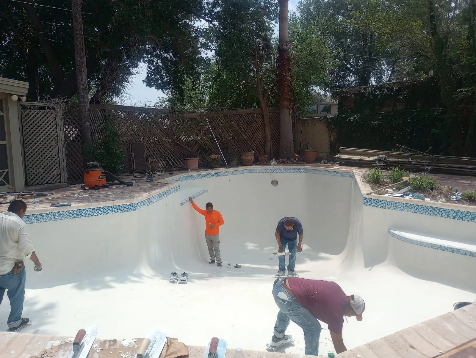 JCW Pools crew troweling fresh plaster across the floor of a drained freeform pool