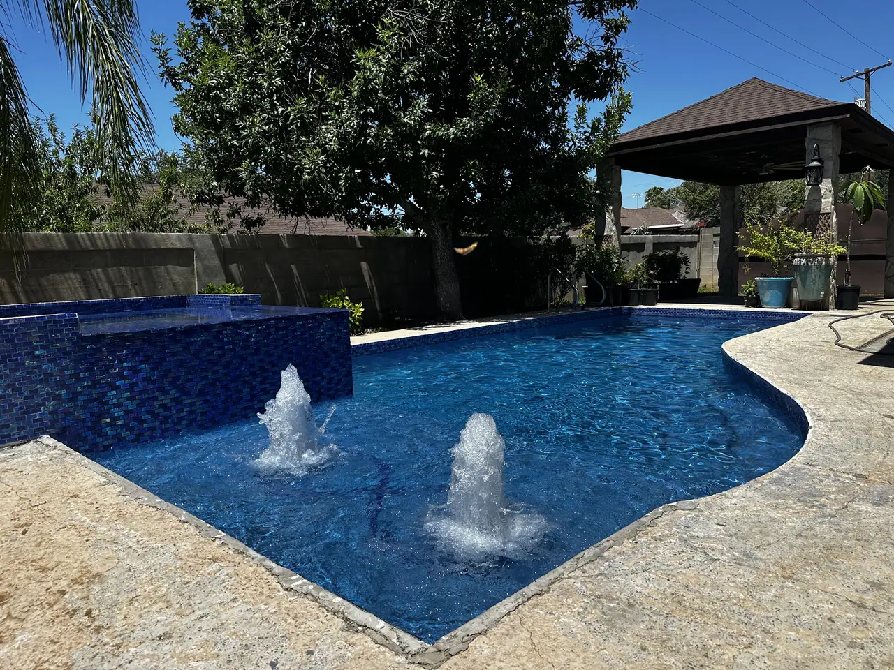 Freeform JCW pool with a dark blue mosaic raised spa and two bubblers running into clear water