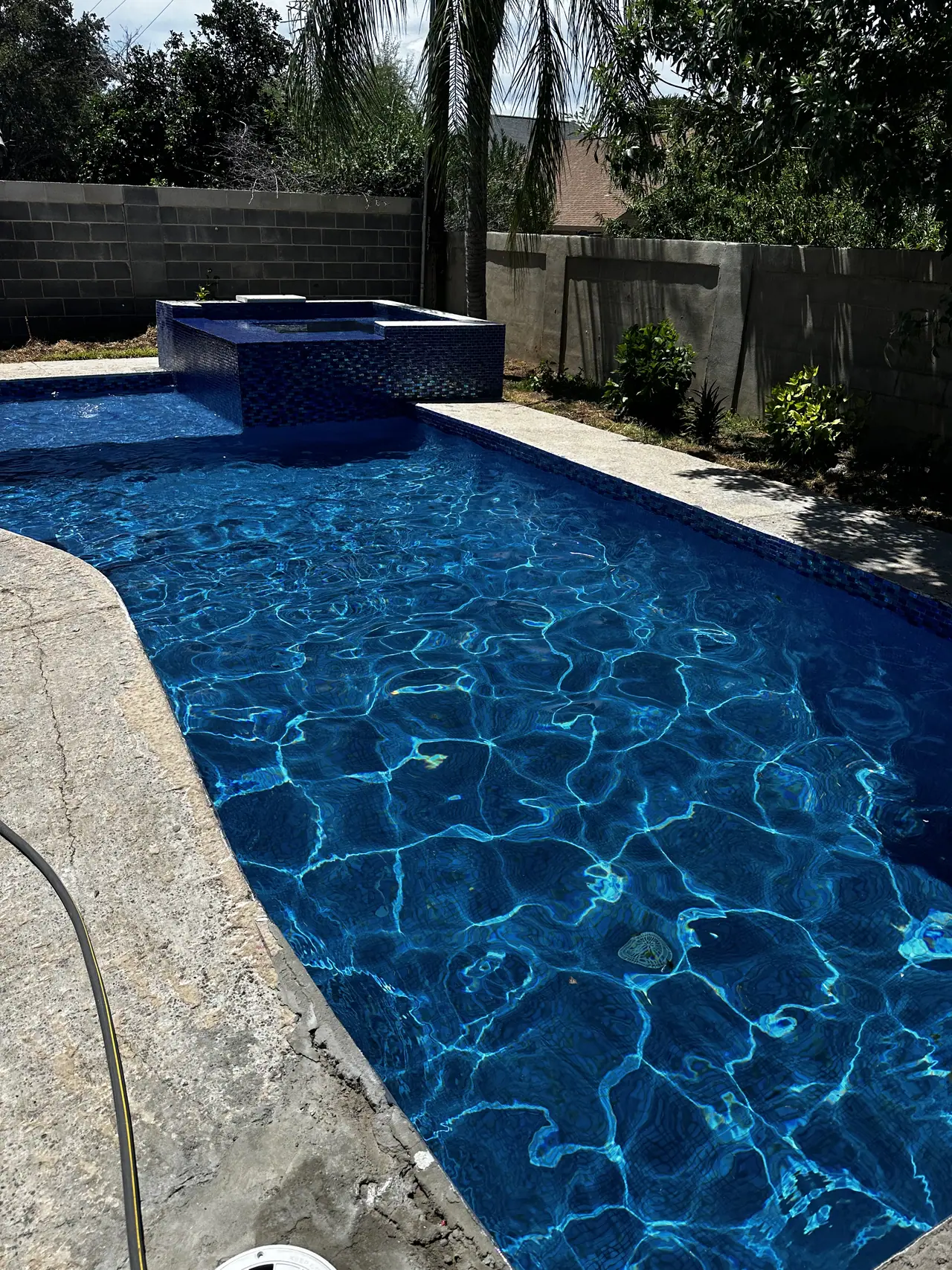 JCW pool with a raised spa and blue mosaic tile beside a stamped concrete deck