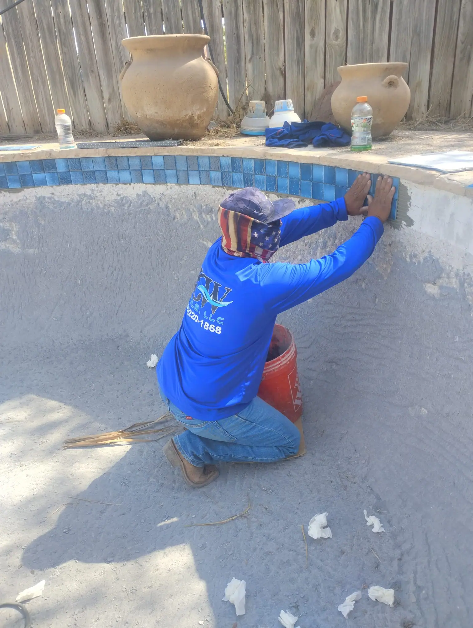 JCW Pools tile setter pressing blue mosaic waterline tile into place on a drained pool